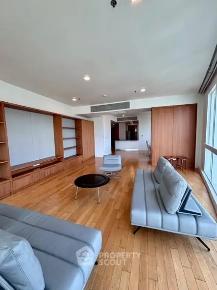 Spacious modern living room with wooden flooring and large windows offering ample natural light.