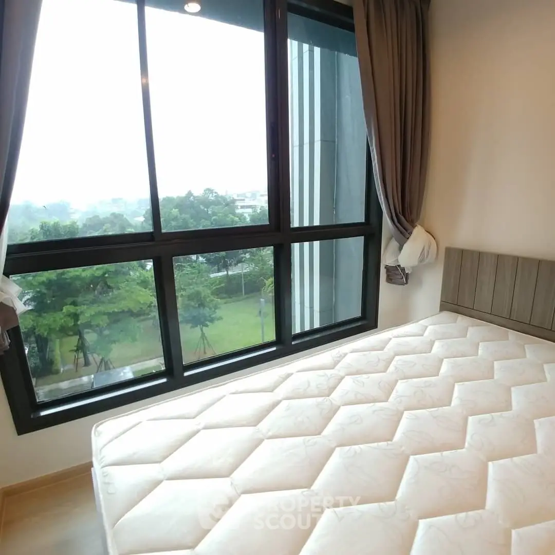 Bright bedroom with large window and garden view, featuring a comfortable mattress.