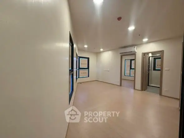 Spacious empty room with wooden flooring and large windows in modern apartment.