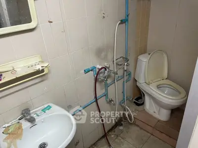 Compact bathroom with basic fixtures and visible plumbing, ideal for renovation projects.