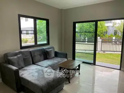 Modern living room with large windows and garden view, featuring a stylish gray sofa and sleek coffee table.