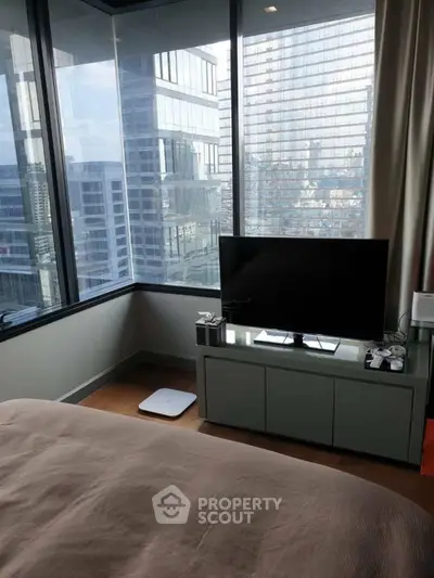 Modern bedroom with city view and sleek TV setup in high-rise apartment.