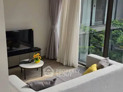 Modern living room with large windows and cozy seating area overlooking greenery.