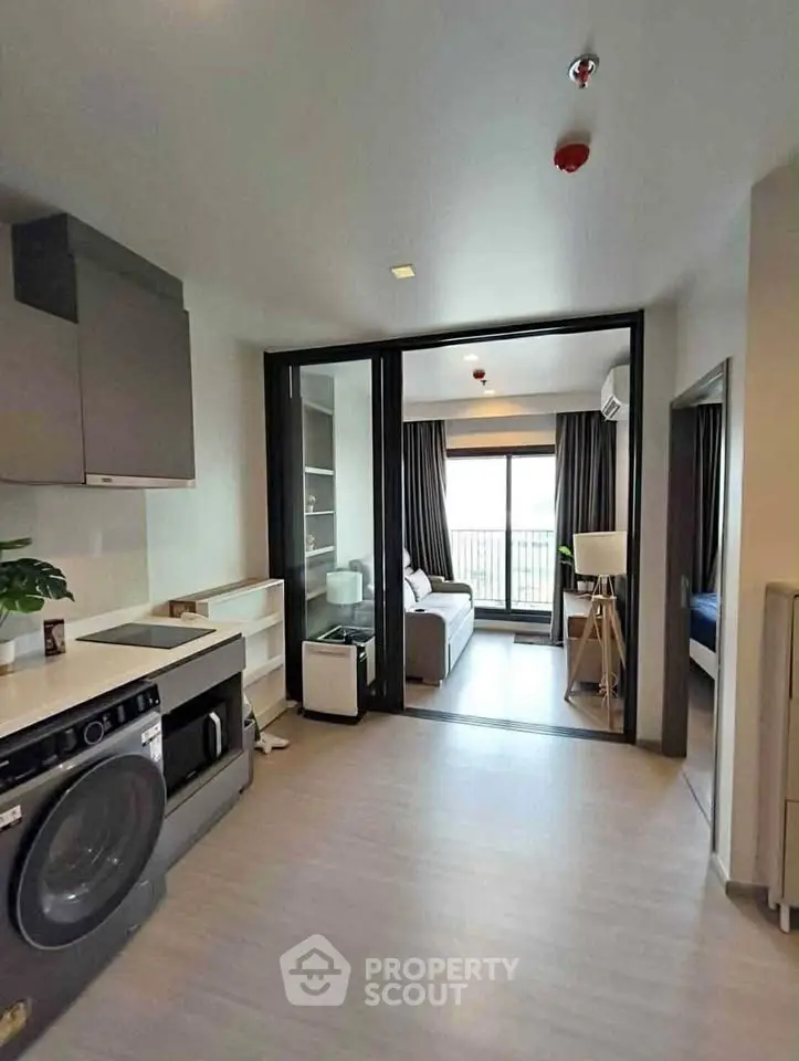 Modern apartment interior with open layout, featuring a kitchen and living area with large windows.