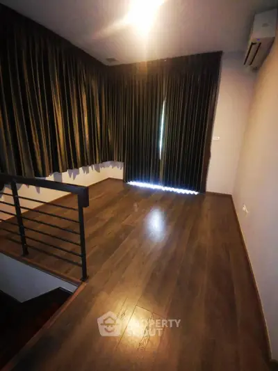 Spacious room with dark wood flooring and elegant curtains, perfect for a cozy living area.