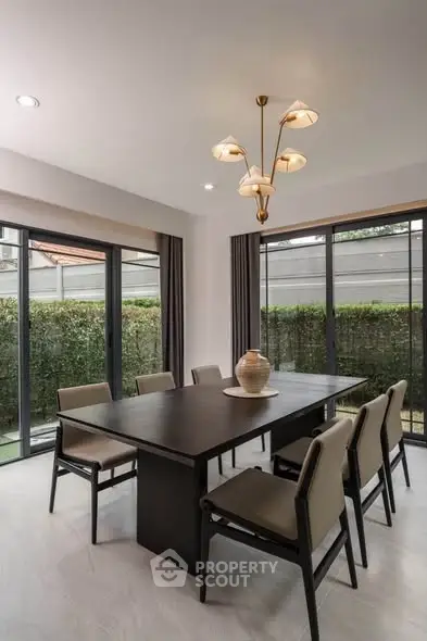 Elegant dining room with modern chandelier and large windows overlooking a lush garden.