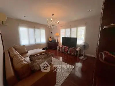Cozy living room with elegant chandelier, leather sofa, and large windows for natural light.