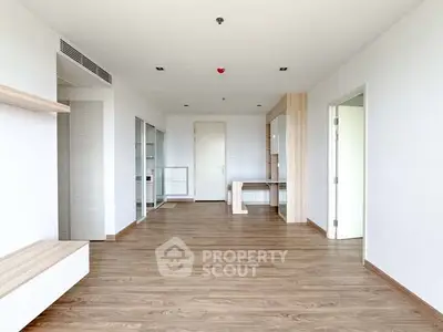 Spacious modern living room with wooden flooring and built-in shelves in a bright apartment.