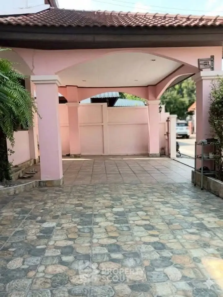 Charming pink exterior with tiled driveway and archway entrance, perfect for welcoming guests.