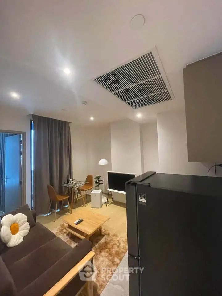 Modern living room with cozy seating and stylish decor, featuring a sleek black refrigerator and ambient lighting.