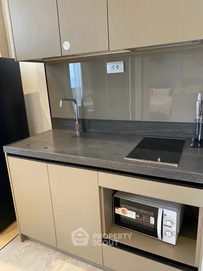 Modern kitchen with sleek cabinetry and built-in microwave, featuring an electric cooktop and stylish faucet.