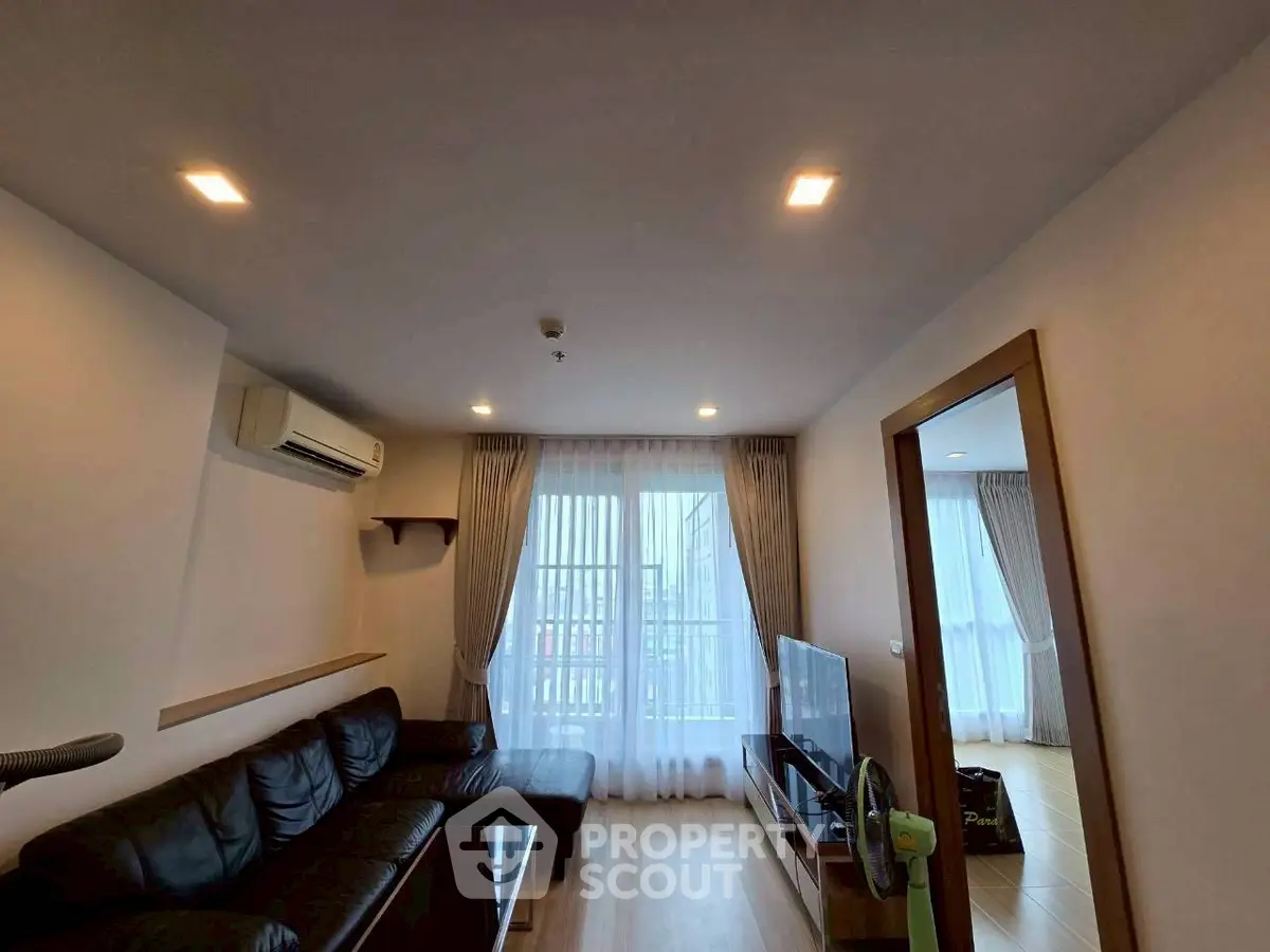 Modern living room with sleek design, featuring a black leather sofa, wooden flooring, and large windows with sheer curtains.