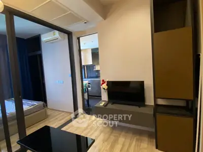 Modern living room with sleek TV setup and view into cozy bedroom and kitchen area.