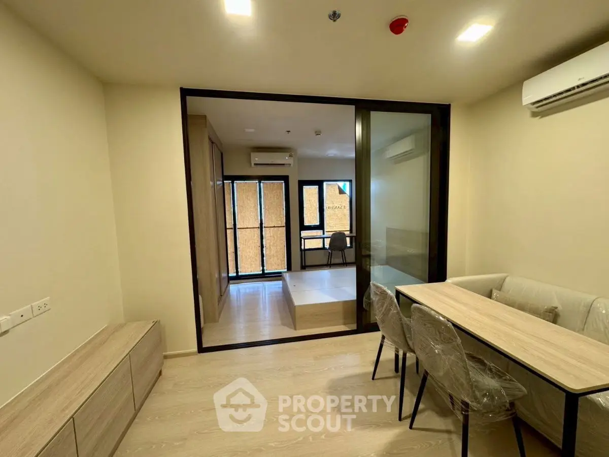 Modern apartment interior with dining area and enclosed balcony, featuring sleek furniture and air conditioning.