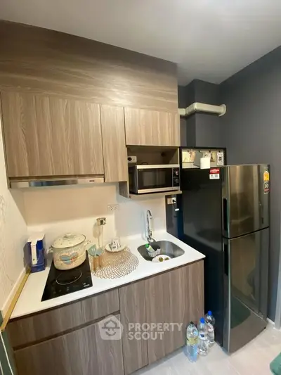 Modern compact kitchen with sleek wooden cabinets and stainless steel appliances in a cozy apartment.