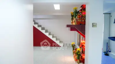 Bright and spacious home interior featuring a clean white aesthetic with a striking red staircase, complemented by vibrant floral decorations.
