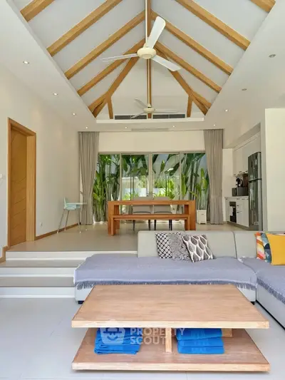 Spacious living room with high ceilings and modern decor, featuring a cozy seating area and large windows overlooking greenery.