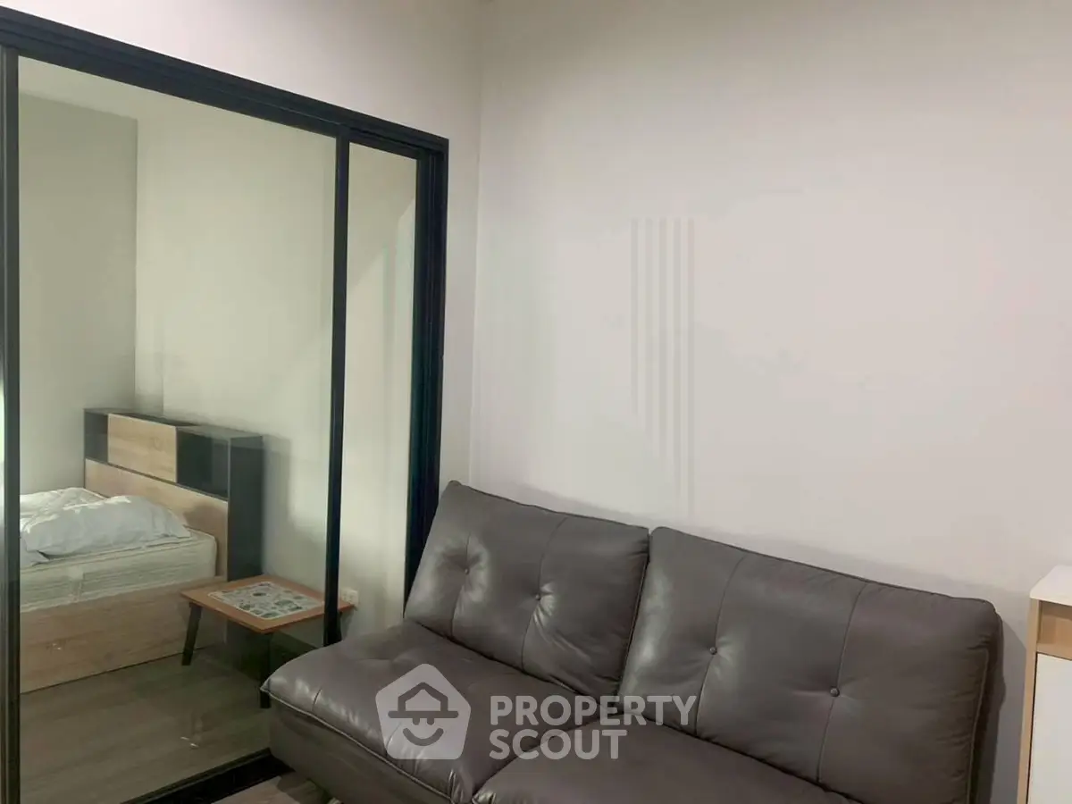 Modern apartment interior with cozy living room and bedroom separated by glass sliding door.