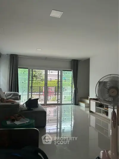 Spacious living room with modern decor and large windows offering natural light and garden view.