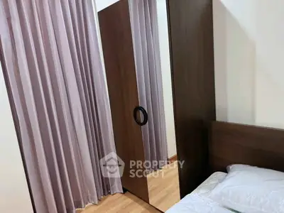 Cozy bedroom with wooden wardrobe and elegant curtains, perfect for a serene living space.