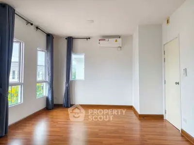 Spacious empty room with wooden flooring and large windows, perfect for customization.