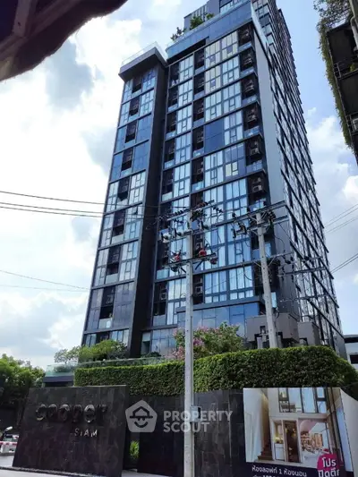 Modern high-rise condominium building with sleek glass facade and lush greenery at entrance.