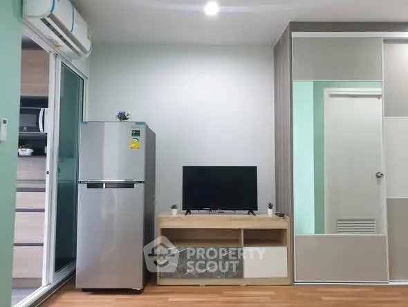 Modern living room with sleek furniture and appliances, featuring a TV and refrigerator.