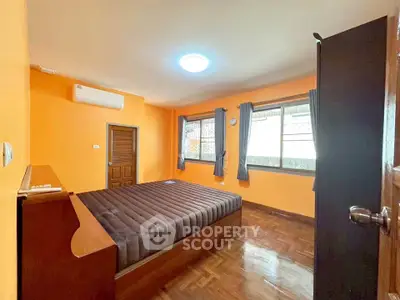 Spacious bedroom with wooden flooring and large windows in a modern apartment.