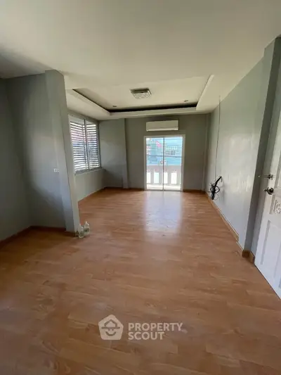 Spacious empty room with wooden flooring and large window for natural light.