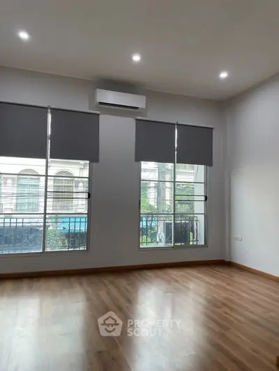 Spacious empty room with wooden flooring and large windows, perfect for customization.