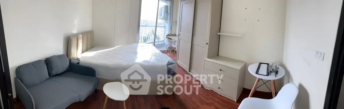 Spacious bedroom with modern furnishings and city view, featuring a cozy sofa and sleek wooden flooring.