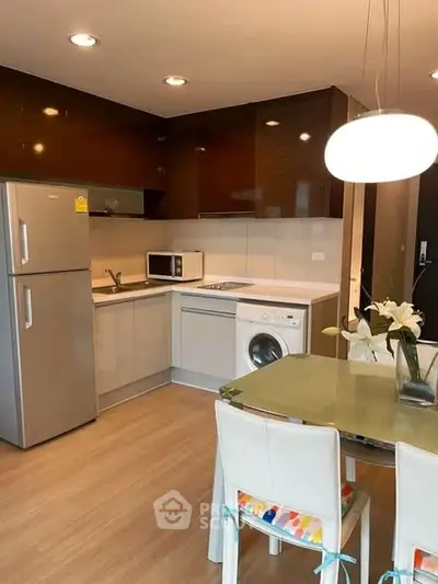 Modern kitchen with sleek appliances and dining area, featuring a washing machine and stylish lighting.