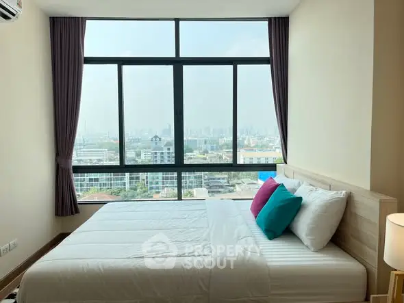 Bright bedroom with large window offering stunning city view, modern decor and colorful pillows.