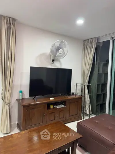 Cozy living room with TV, wooden furniture, and elegant curtains.