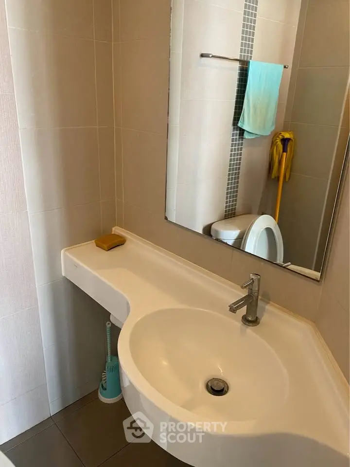 Modern bathroom with sleek sink and mirror, featuring neutral tiles and contemporary fixtures.