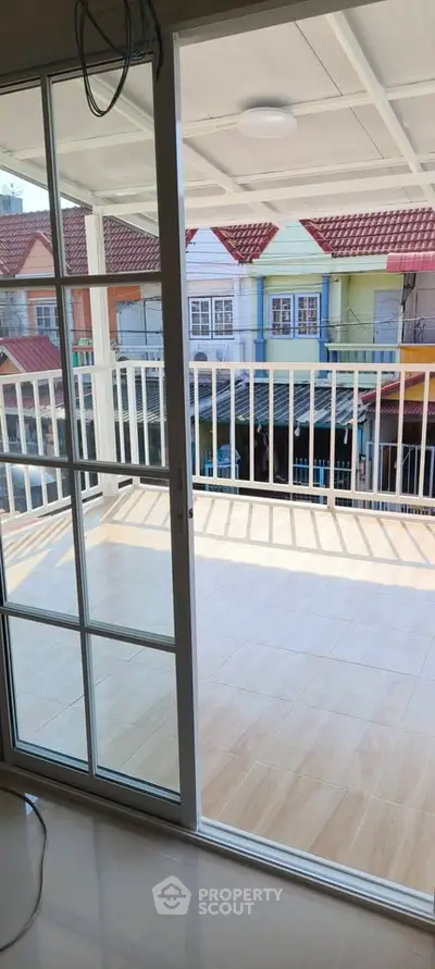Spacious balcony with sliding glass doors and tiled flooring, offering a view of colorful neighboring houses.