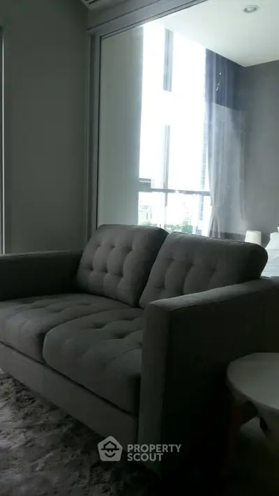 Modern living room with stylish gray sofa and large windows offering natural light.
