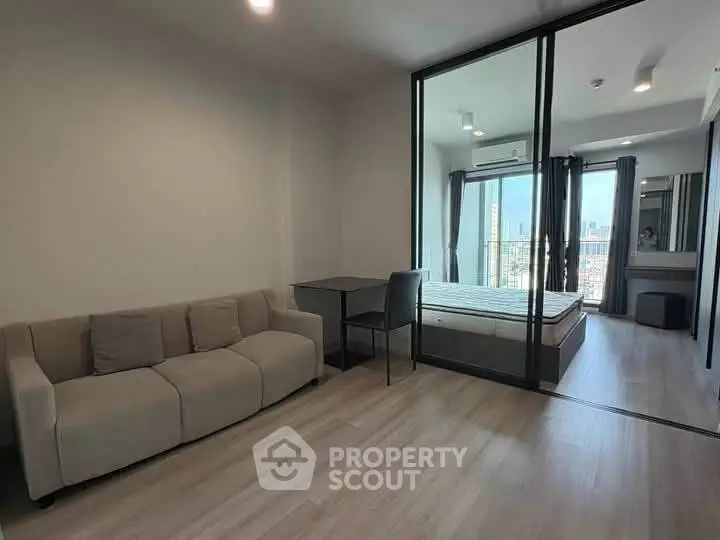 Modern studio apartment with glass partition, cozy sofa, and city view balcony.
