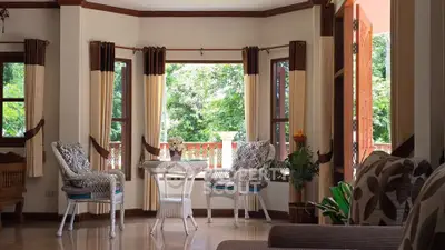Charming living room with large windows and elegant decor, offering a serene garden view.
