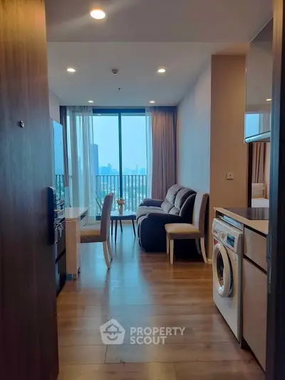 Modern living room with city view, featuring cozy seating and in-unit washing machine.