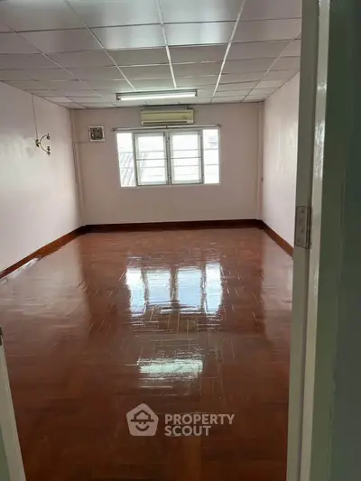 Spacious empty room with polished wooden floors and large windows.