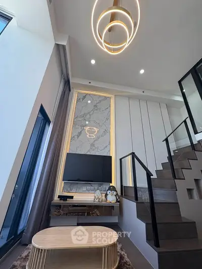 Modern living room with high ceiling, stylish lighting, and sleek staircase in a contemporary home.
