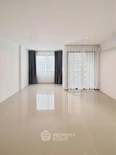 Spacious empty room with glossy tiled floor and large windows with curtains.