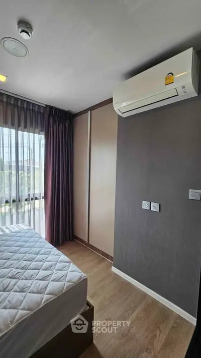 Modern bedroom with air conditioning and large window, featuring stylish curtains and wooden flooring.
