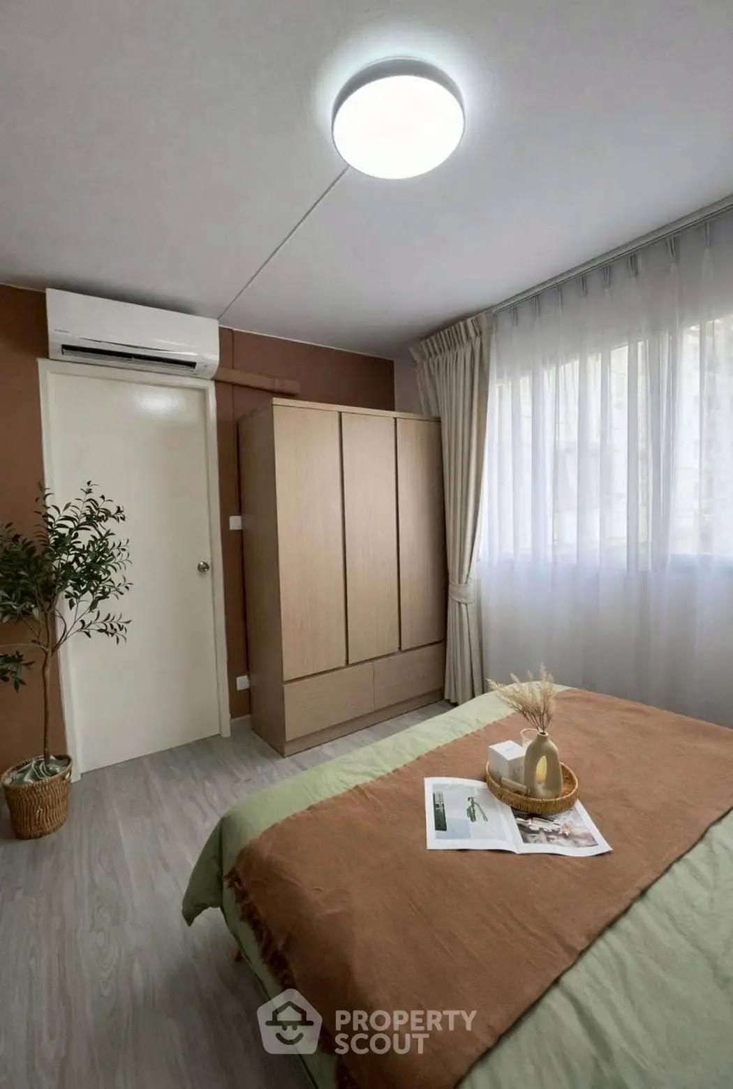 Cozy bedroom with modern decor, featuring a large window, wardrobe, and air conditioning unit.