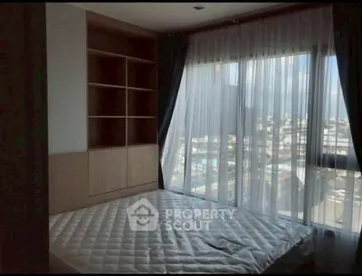 Spacious bedroom with large window offering city view and built-in shelves.