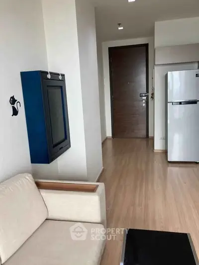 Modern apartment interior with sleek wooden flooring, cozy sofa, and stainless steel fridge near entrance.