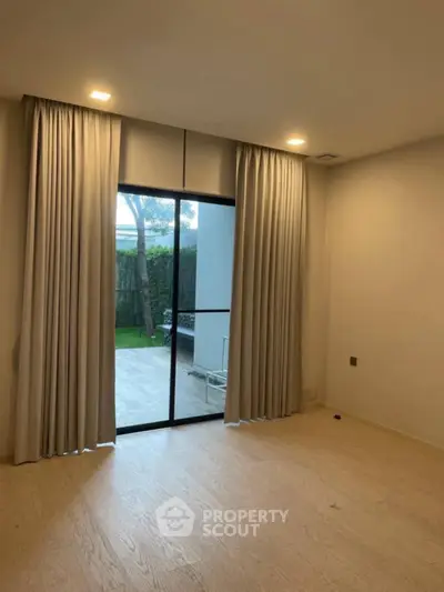 Spacious room with large sliding glass doors leading to a private garden patio, featuring elegant floor-to-ceiling curtains.