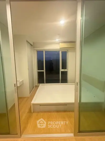 Modern bedroom with sliding glass doors and wooden flooring, featuring a minimalist design and ample natural light.