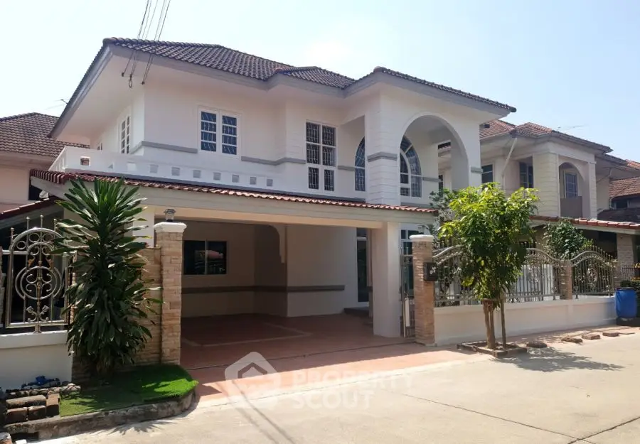 Elegant two-story house with arched entrance and spacious driveway in sunny neighborhood.